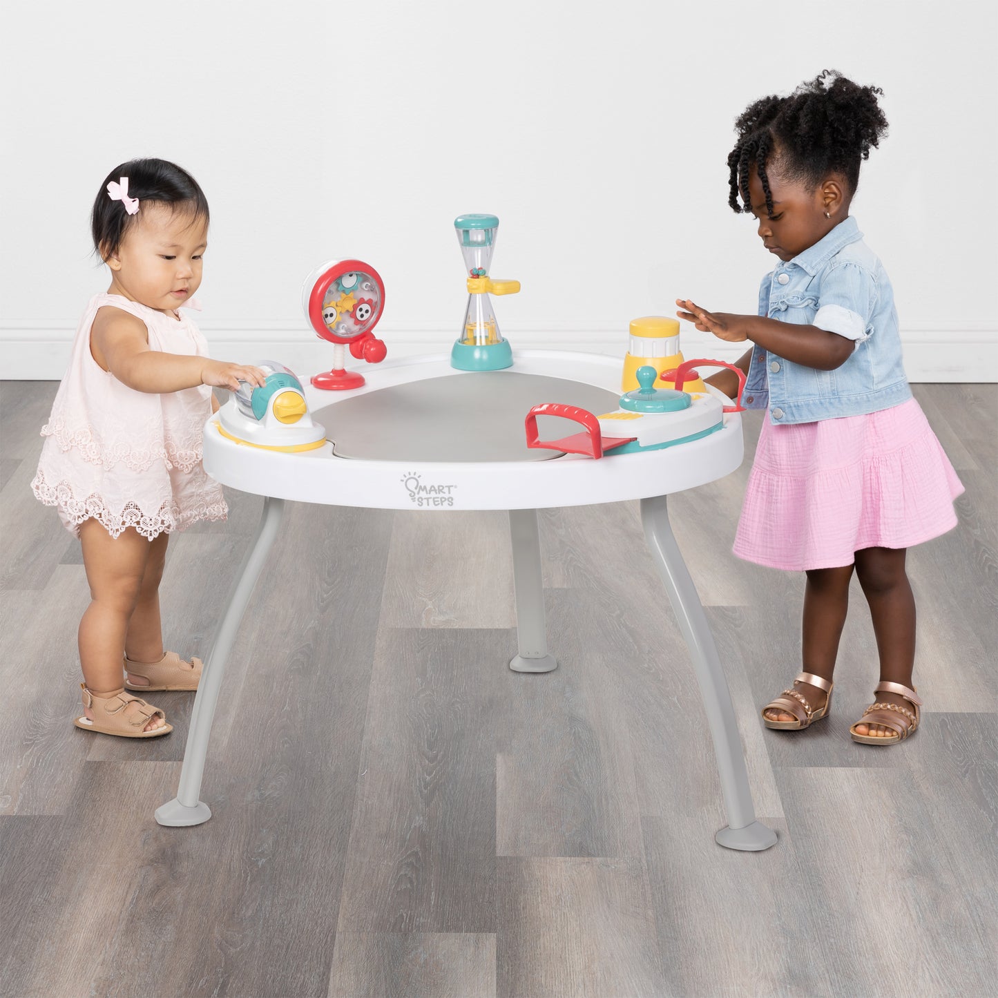 Two children using the Smart Steps Hop N' Discover 3-in-1 Activity Center as a table to play with the toys