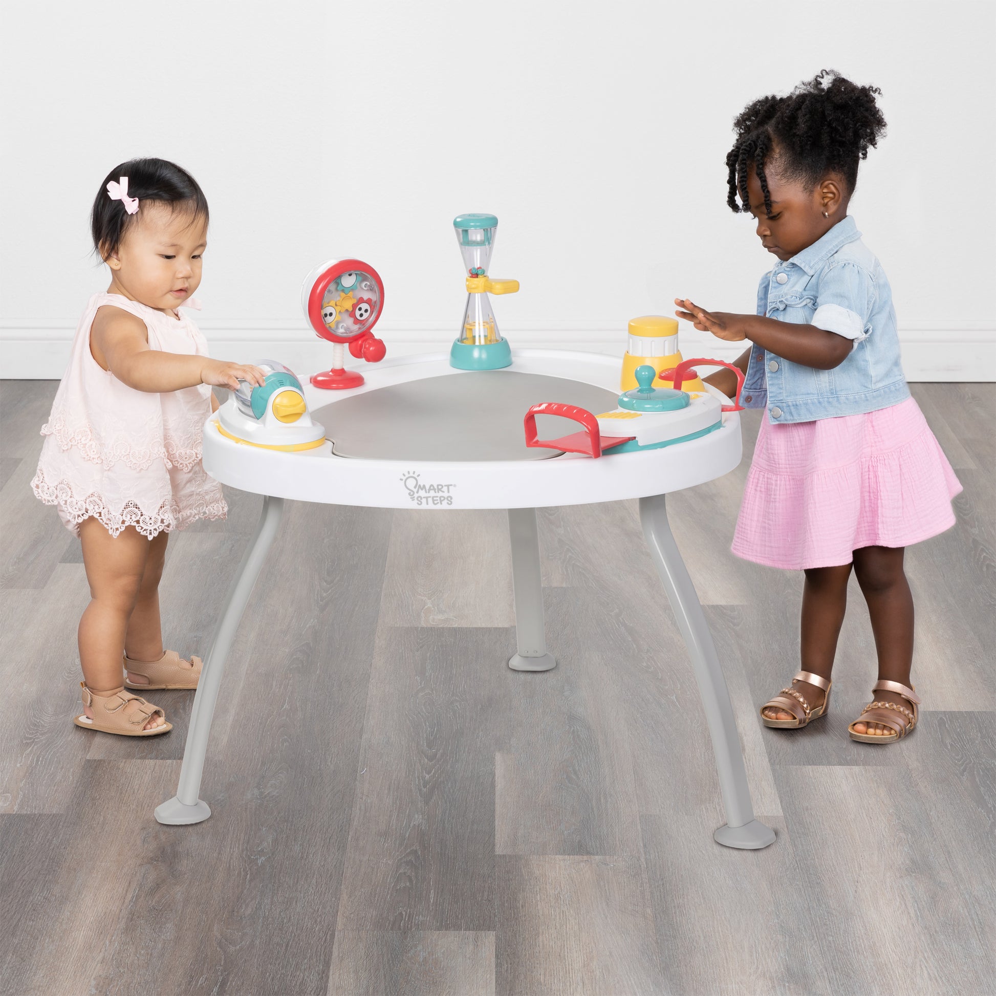Two children using the Smart Steps Hop N' Discover 3-in-1 Activity Center as a table to play with the toys