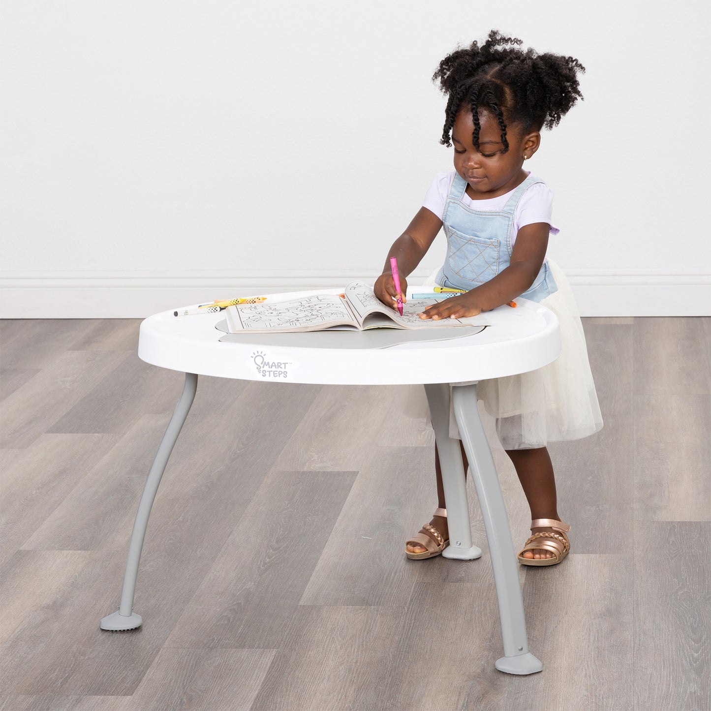 A girl is using the Smart Steps Hop N' Discover 3-in-1 Activity Center as a table to color her book